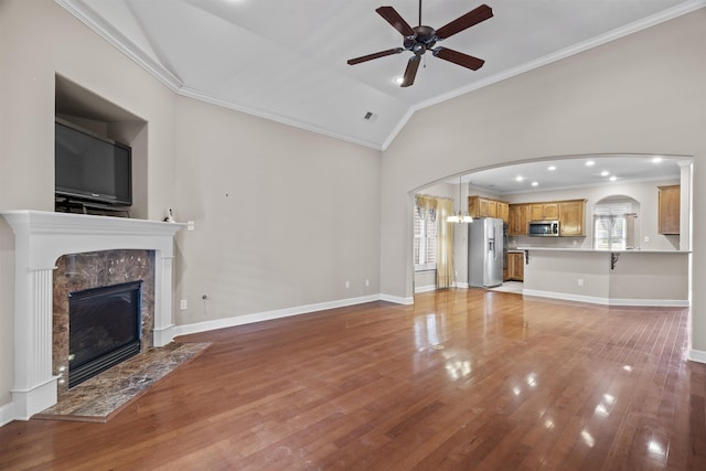 unfurnished living room featuring crown molding, vaulted ceiling, ceiling fan, arched walkways, and a high end fireplace