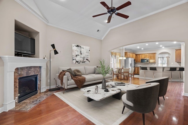 living area featuring ornamental molding, arched walkways, light wood-style floors, a ceiling fan, and lofted ceiling