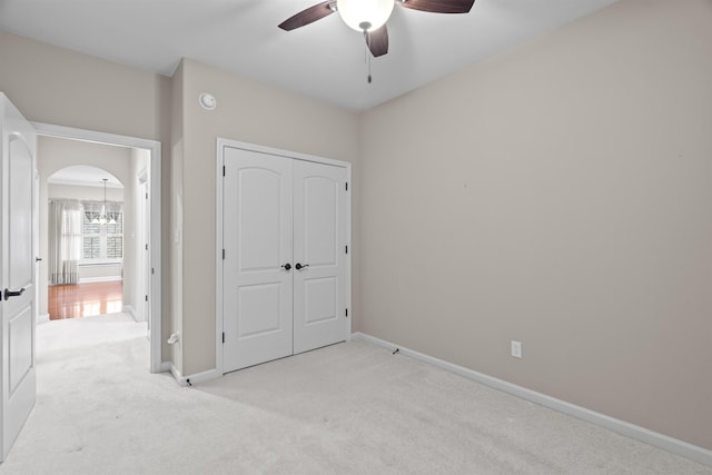 unfurnished bedroom featuring light colored carpet, a closet, baseboards, arched walkways, and a chandelier