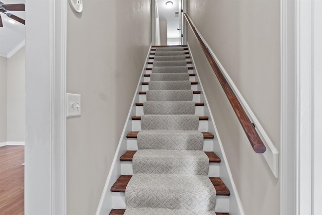 stairway featuring a ceiling fan, baseboards, wood finished floors, and a high ceiling