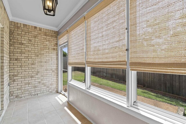 unfurnished sunroom featuring crown molding, tile patterned floors, brick wall, and a chandelier