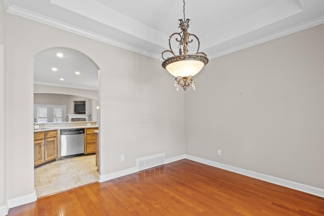 empty room featuring arched walkways, light wood-style floors, ornamental molding, a tray ceiling, and recessed lighting