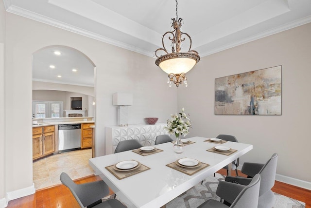 dining space featuring arched walkways, ornamental molding, light wood-style flooring, a raised ceiling, and recessed lighting
