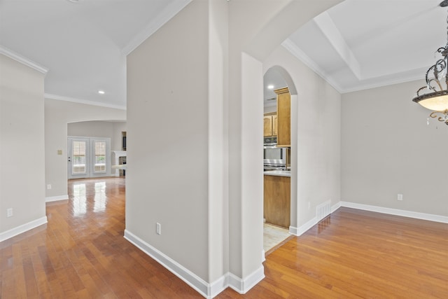 hallway featuring ornamental molding, arched walkways, light wood-style flooring, a chandelier, and baseboards