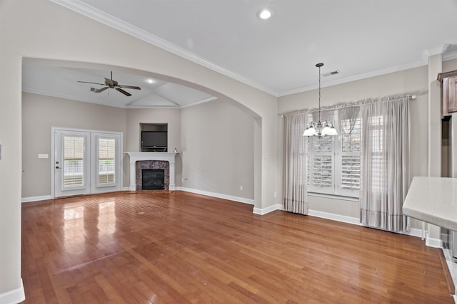 unfurnished living room with a chandelier, light wood-style floors, arched walkways, a ceiling fan, and baseboards
