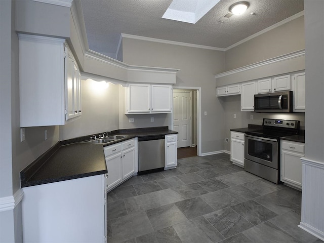 kitchen with stainless steel appliances, a sink, a skylight, dark countertops, and white cabinets