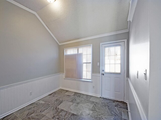 doorway featuring lofted ceiling, a textured ceiling, crown molding, wainscoting, and healthy amount of natural light