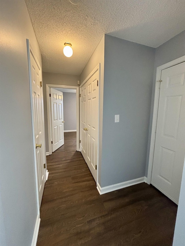 corridor with baseboards, dark wood-type flooring, and a textured ceiling