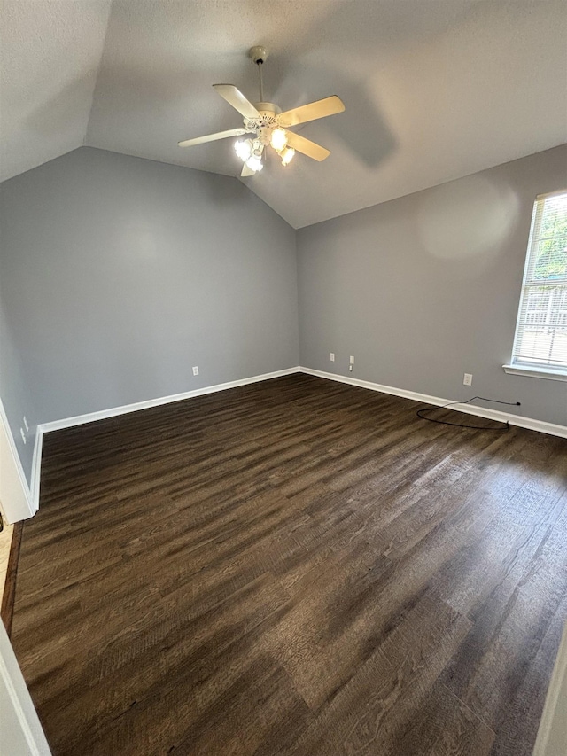 empty room featuring ceiling fan, lofted ceiling, baseboards, and dark wood-type flooring