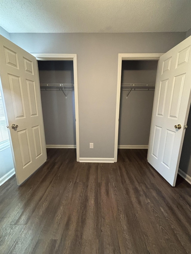 unfurnished bedroom with dark wood finished floors, two closets, baseboards, and a textured ceiling