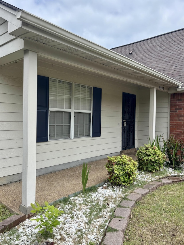 view of exterior entry with roof with shingles and a porch