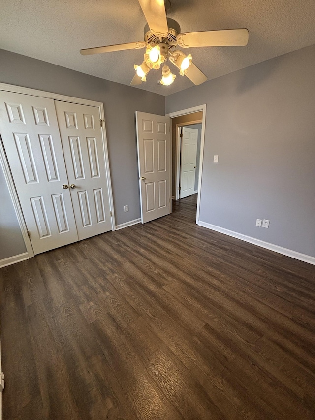unfurnished bedroom featuring dark wood finished floors, baseboards, a closet, ceiling fan, and a textured ceiling