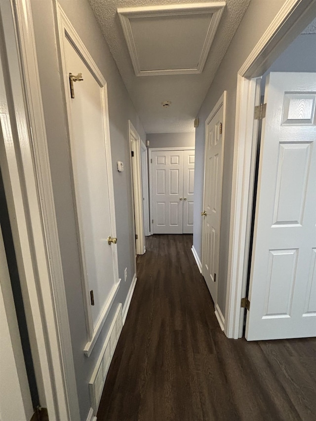 hallway featuring dark wood-type flooring, attic access, and baseboards