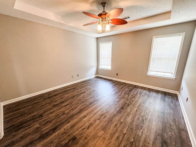 unfurnished room featuring a textured ceiling, a raised ceiling, dark wood finished floors, a ceiling fan, and baseboards