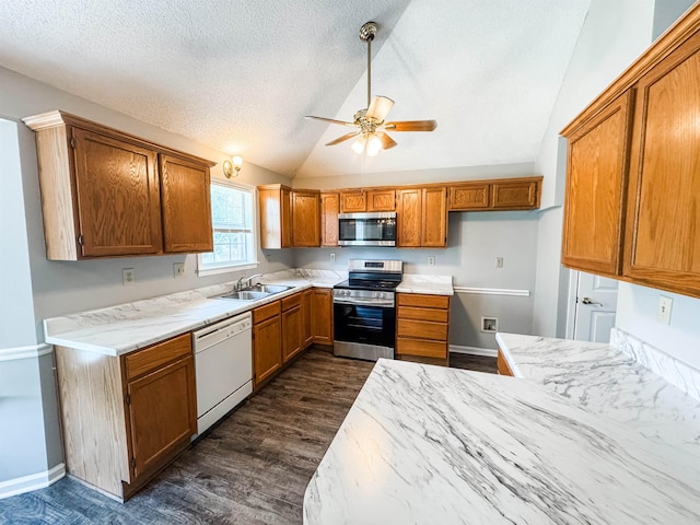 kitchen with appliances with stainless steel finishes, a sink, vaulted ceiling, brown cabinetry, and dark wood-style flooring