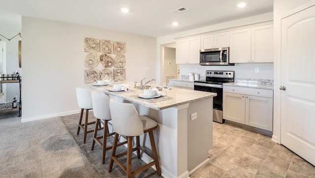 8005 Royster Creek Dr E, Millington, TN 38053 - kitchen featuring stainless steel appliances, an island with sink, a kitchen bar, light stone counters, and recessed lighting