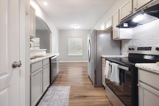 kitchen with stainless steel appliances, under cabinet range hood, light wood-style floors, baseboards, and arched walkways