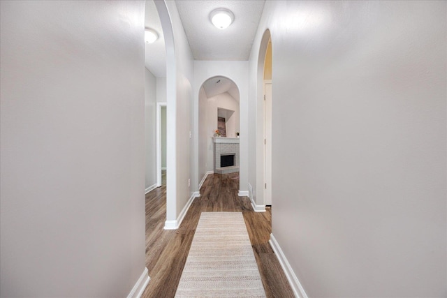 hallway featuring wood finished floors, baseboards, and arched walkways