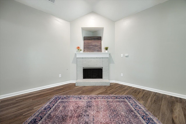 unfurnished living room with wood finished floors, a brick fireplace, baseboards, and lofted ceiling
