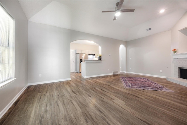 unfurnished living room featuring ceiling fan, arched walkways, wood finished floors, lofted ceiling, and baseboards