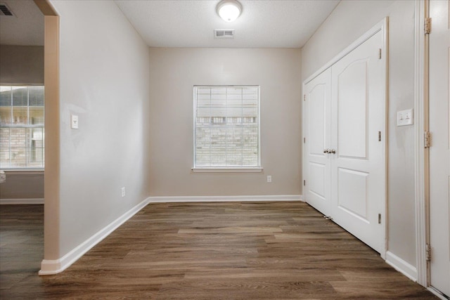 unfurnished bedroom featuring multiple windows, wood finished floors, a closet, and baseboards