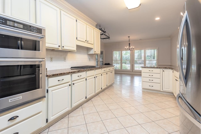 1625 Autumn Tree Cv, Memphis, TN 38016 - kitchen featuring appliances with stainless steel finishes, ornamental molding, a chandelier, light tile patterned floors, and dark stone countertops
