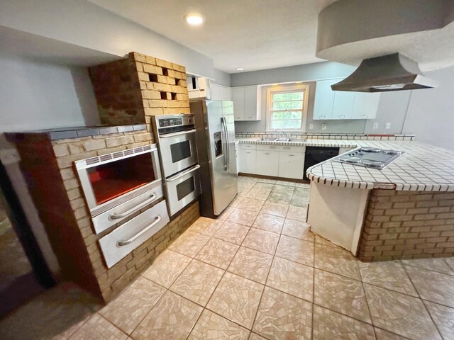 3751 Lakewood Dr N, Memphis, TN 38128 - kitchen with tile countertops, appliances with stainless steel finishes, exhaust hood, white cabinets, and a peninsula
