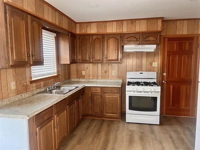 760 E Mckellar Ave, Memphis, TN 38106 - kitchen featuring white range with gas stovetop, under cabinet range hood, a sink, wooden walls, and brown cabinets