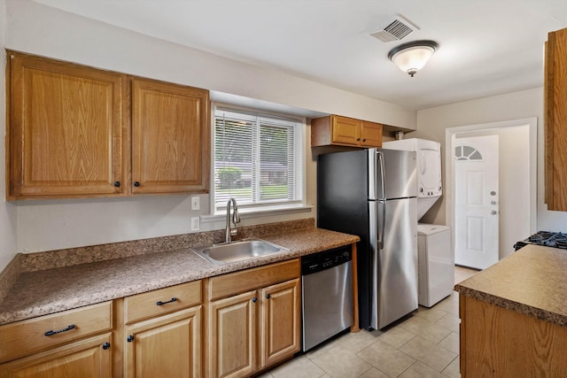 307 Melita Rd, Memphis, TN 38120 - kitchen with appliances with stainless steel finishes, a sink, stacked washer and clothes dryer, light tile patterned flooring, and dark countertops
