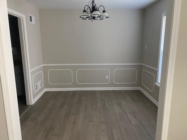 4947 Demeter Cv, Memphis, TN 38118 - unfurnished dining area with a chandelier, dark wood-style floors, wainscoting, and a decorative wall