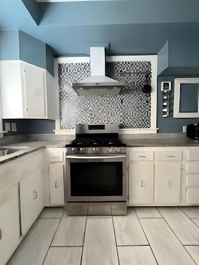 929 N Watkins St, Memphis, TN 38107 - kitchen featuring stainless steel range with gas stovetop, wall chimney range hood, white cabinetry, and backsplash