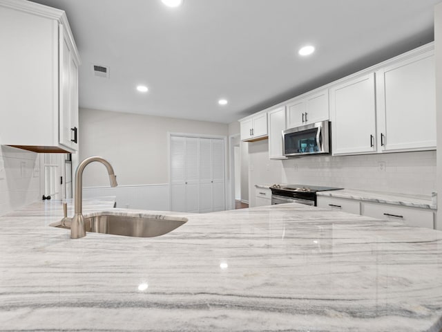 712 Lawncrest Cv, Collierville, TN 38017 - kitchen featuring stainless steel appliances, a sink, light stone countertops, tasteful backsplash, and white cabinetry
