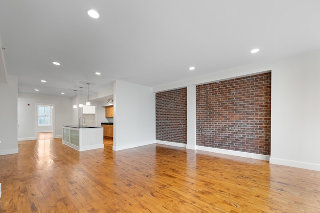123 Court Ave Unit 401, Memphis, TN 38103 - unfurnished living room with light wood-style flooring, a sink, baseboards, recessed lighting, and brick wall