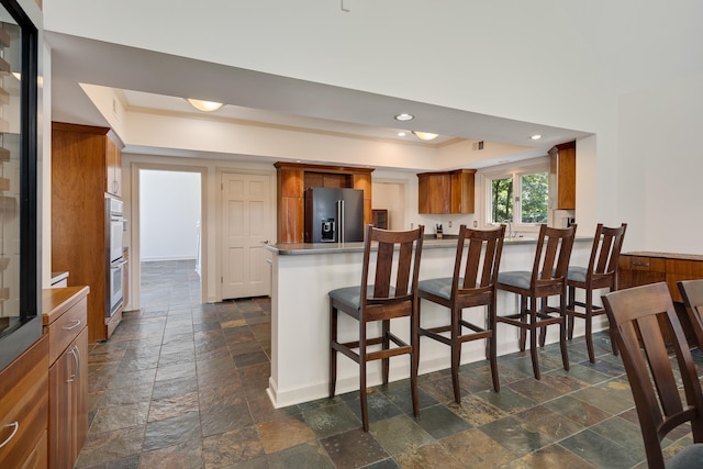 236 Riveredge Cv, Memphis, TN 38018 - kitchen featuring stone tile flooring, high end refrigerator, a tray ceiling, brown cabinetry, and a peninsula