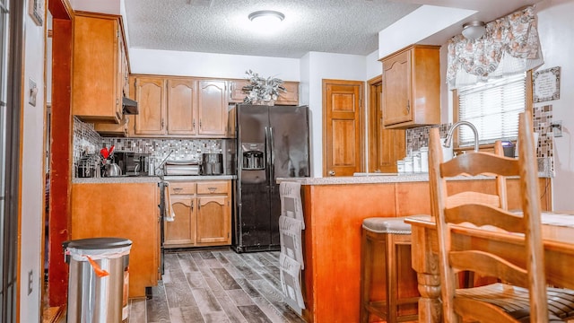4431 Green Creek Dr, Memphis, TN 38125 - kitchen featuring black fridge with ice dispenser, a textured ceiling, a peninsula, tasteful backsplash, and wood finished floors