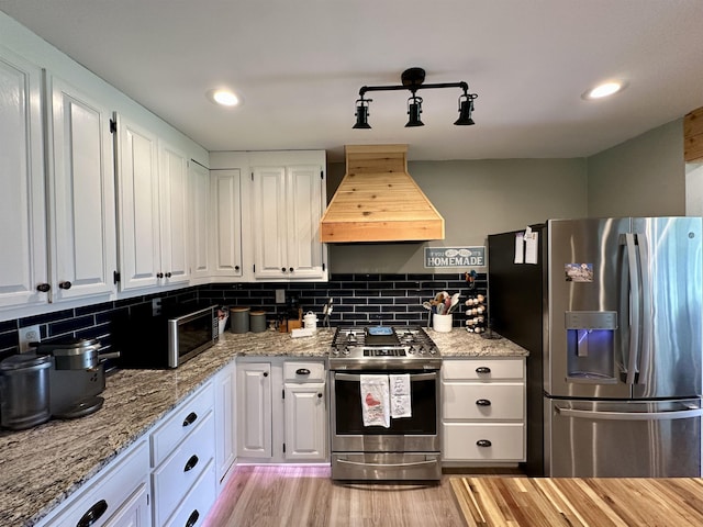 520 Jernigan Dr, Somerville, TN 38068 - kitchen with appliances with stainless steel finishes, custom exhaust hood, white cabinetry, light wood-style floors, and backsplash