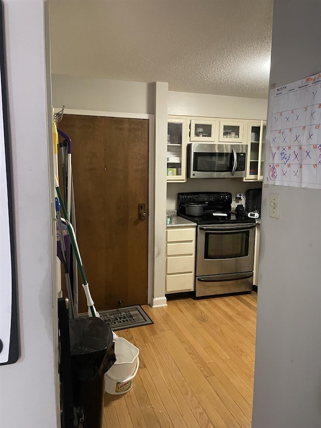 109 N Main St Unit 1202, Memphis, TN 38103 - kitchen with stainless steel appliances, light wood-type flooring, glass insert cabinets, a textured ceiling, and white cabinetry
