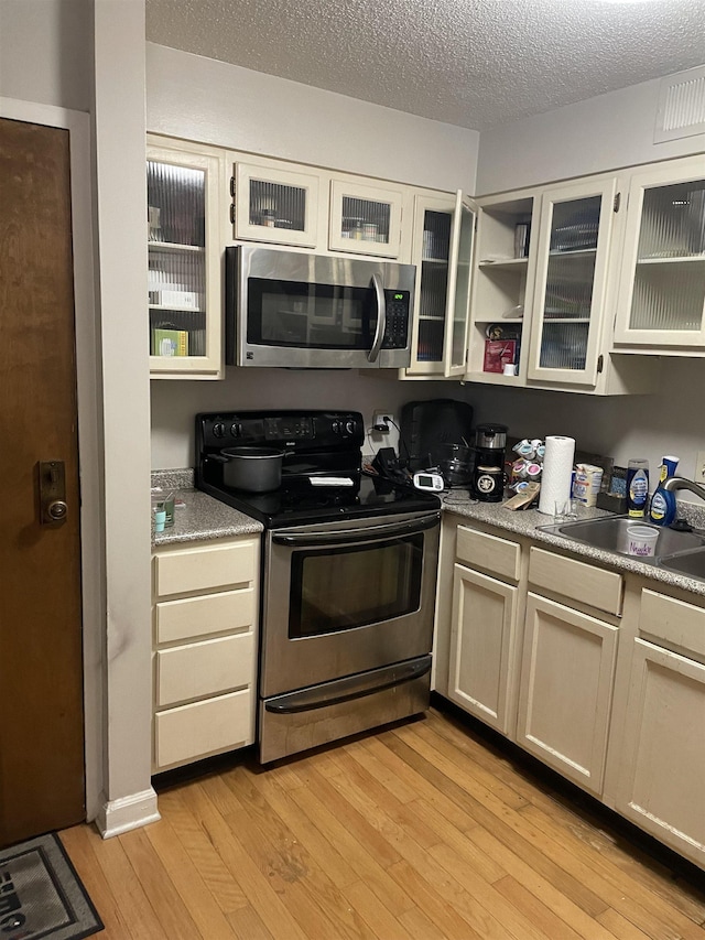 109 N Main St Unit 1202, Memphis, TN 38103 - kitchen with stainless steel appliances, light wood-type flooring, glass insert cabinets, and a textured ceiling