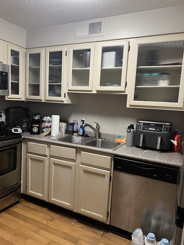 109 N Main St Unit 1202, Memphis, TN 38103 - kitchen with stainless steel appliances, light wood finished floors, glass insert cabinets, and a textured ceiling