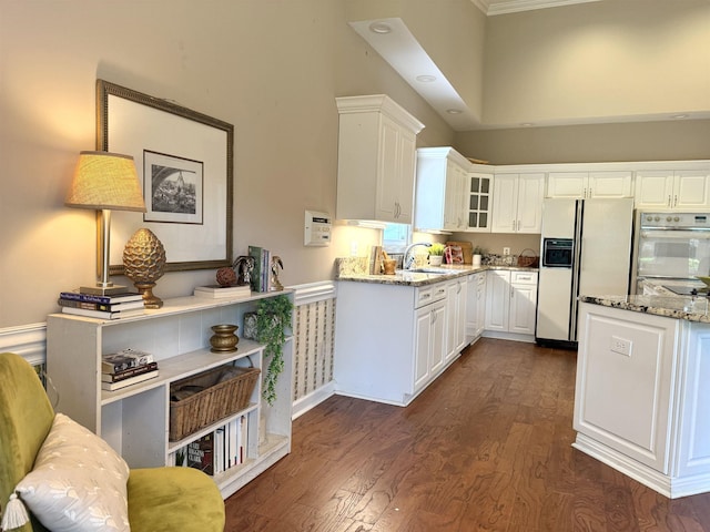 7598 Fairway Forest Dr E, Memphis, TN 38016 - kitchen with white appliances, light stone countertops, dark wood-style flooring, white cabinetry, and glass insert cabinets