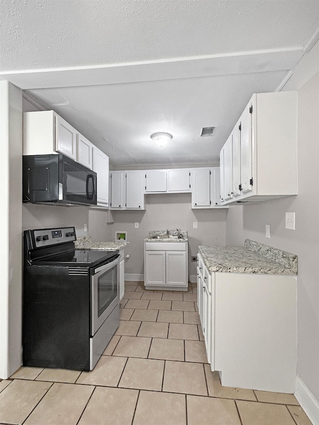 1644 N Graham St, Memphis, TN 38108 - kitchen with stainless steel electric stove, black microwave, light tile patterned floors, and white cabinetry