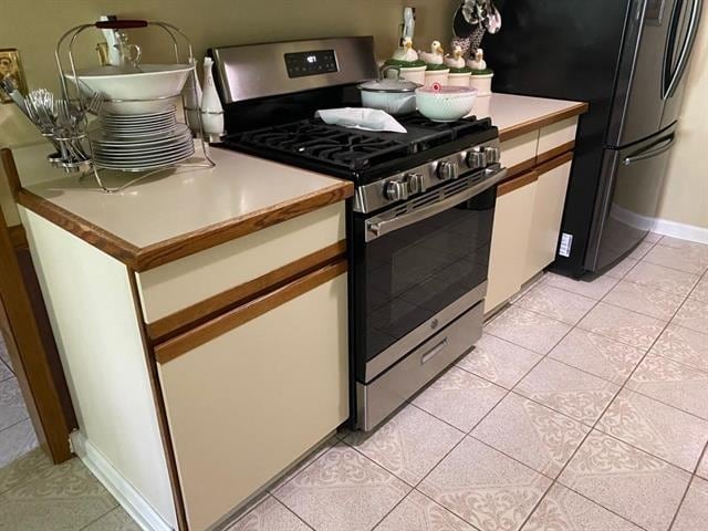 7148 Tranquil Creek Dr, Memphis, TN 38125 - kitchen with stainless steel gas range oven, light tile patterned flooring, white cabinetry, freestanding refrigerator, and light countertops