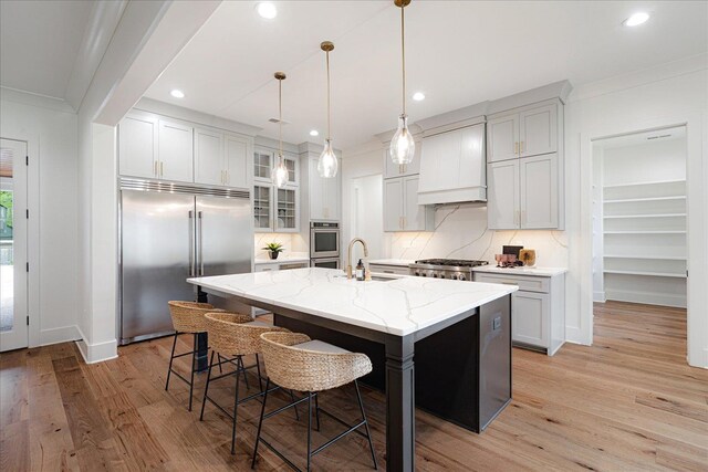 2486 E Allelon Rd E, Germantown, TN 38138 - kitchen featuring stainless steel appliances, premium range hood, light wood-style floors, tasteful backsplash, and an island with sink
