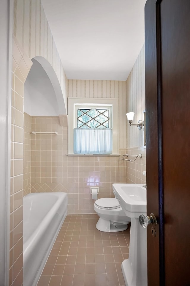2067 Hallwood Dr, Memphis, TN 38107 - full bath featuring a bathtub, tile patterned floors, wallpapered walls, tile walls, and a wainscoted wall