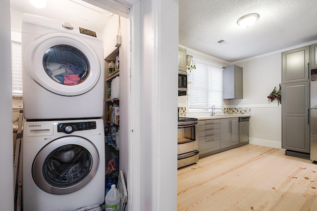569 Lundee Pl, Memphis, TN 38111 - washroom featuring stacked washer and clothes dryer, light wood-style floors, ornamental molding, and a textured ceiling