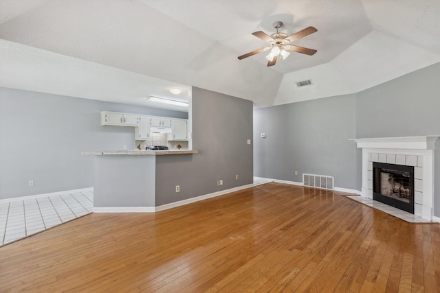 2766 Fletcher View Dr, Memphis, TN 38016 - unfurnished living room featuring ceiling fan, light wood-type flooring, a tiled fireplace, and lofted ceiling