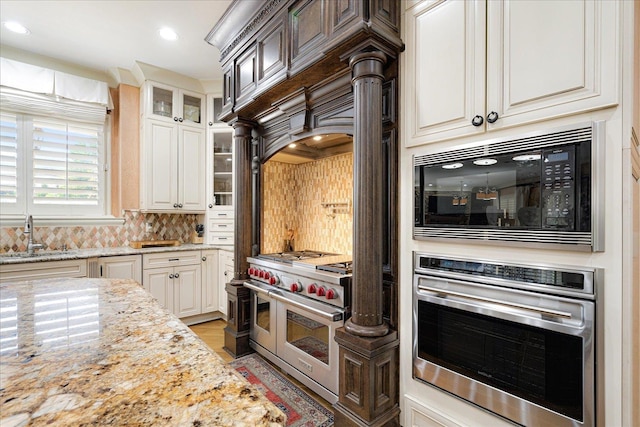269 N Monterey Farms Cv, Collierville, TN 38017 - kitchen featuring appliances with stainless steel finishes, light stone counters, glass insert cabinets, tasteful backsplash, and recessed lighting