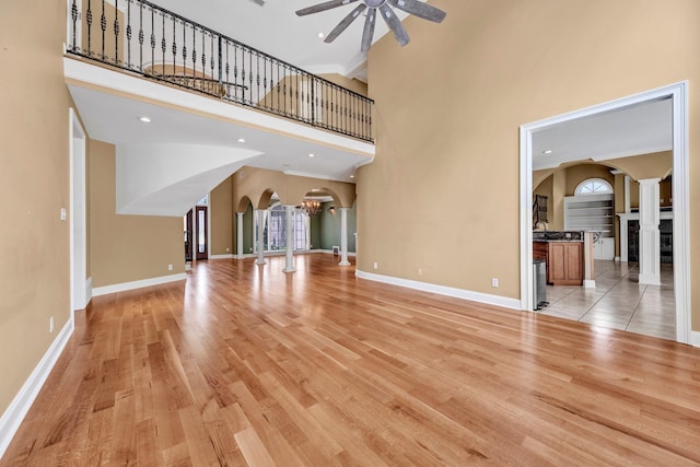 1062 Center Ridge Rd, Collierville, TN 38017 - unfurnished living room featuring arched walkways, decorative columns, a ceiling fan, light wood-style floors, and a towering ceiling