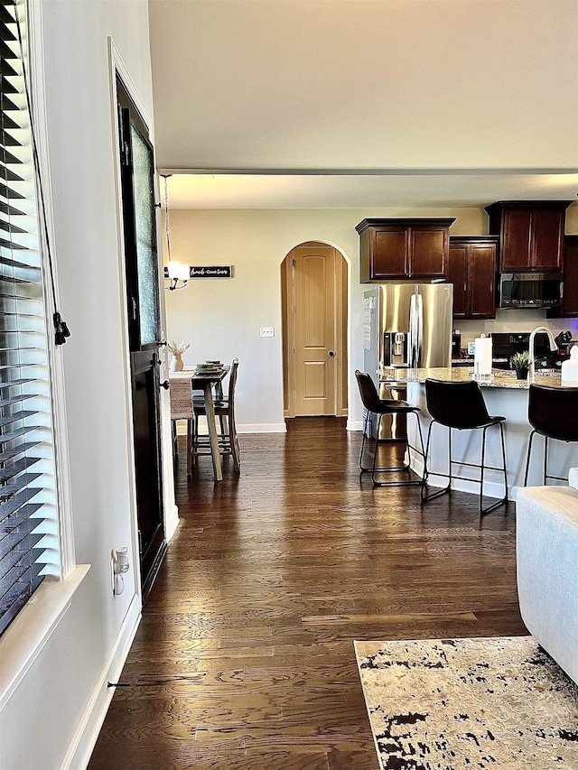 8334 Stonecrest Dr W, Olive Branch, MS 38654 - kitchen featuring appliances with stainless steel finishes, dark brown cabinets, a kitchen breakfast bar, arched walkways, and dark wood-style flooring