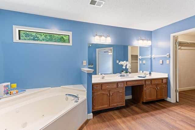 1504 Teal Wing Ln, Memphis, TN 38016 - bathroom with wood finished floors, a whirlpool tub, double vanity, a spacious closet, and a textured ceiling